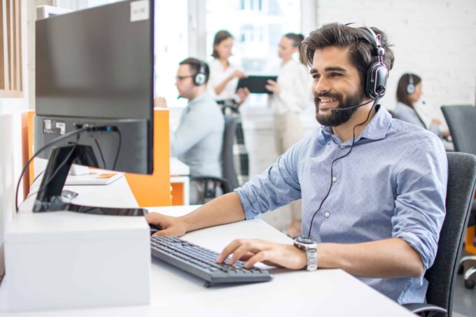 Support technician with headset providing IT assistance in a busy office environment.