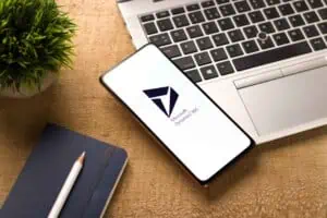 Smartphone displaying Microsoft Dynamics 365 logo with laptop and notebook on wooden desk.