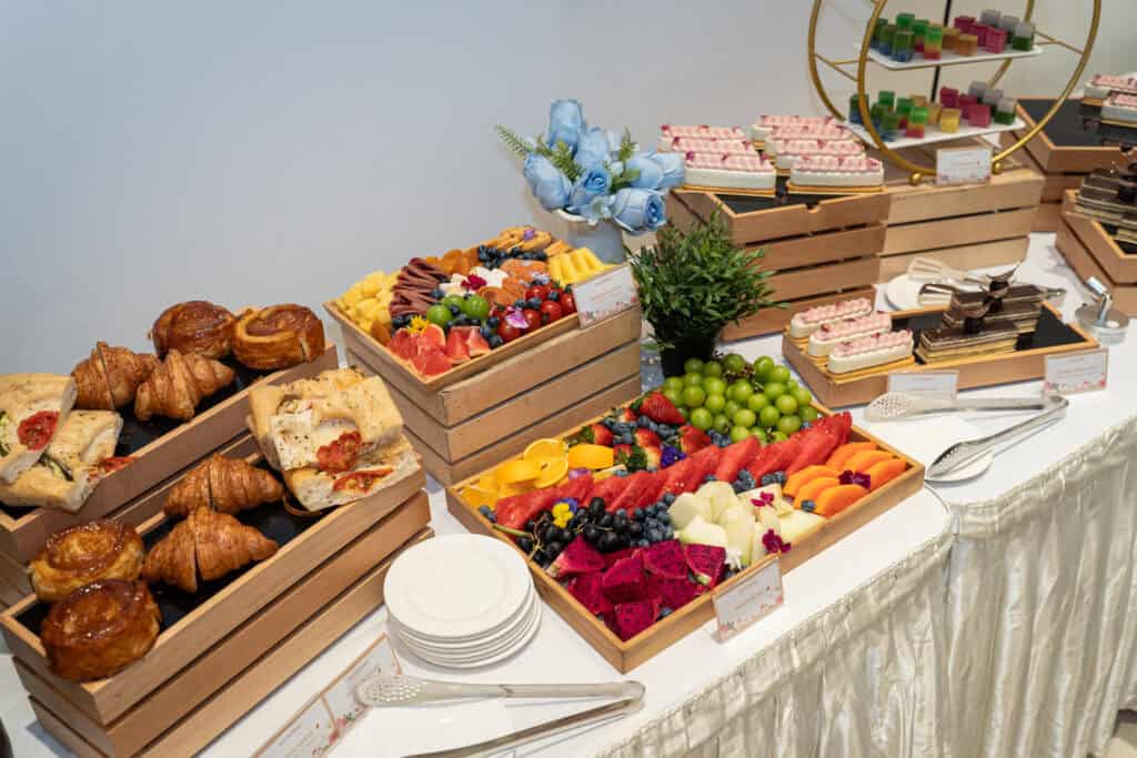 An assortment of desserts such as fruit platter, grazing platter, croissant, cake served on wooden crates for wedding catering