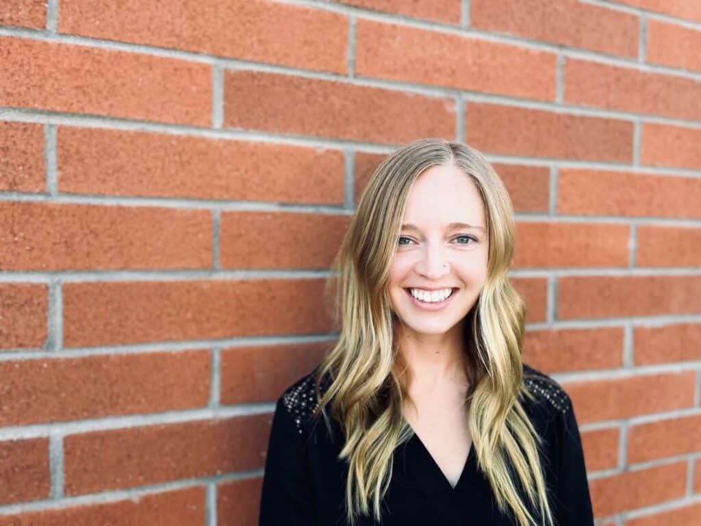 Smiling female physical therapist standing against brick wall.