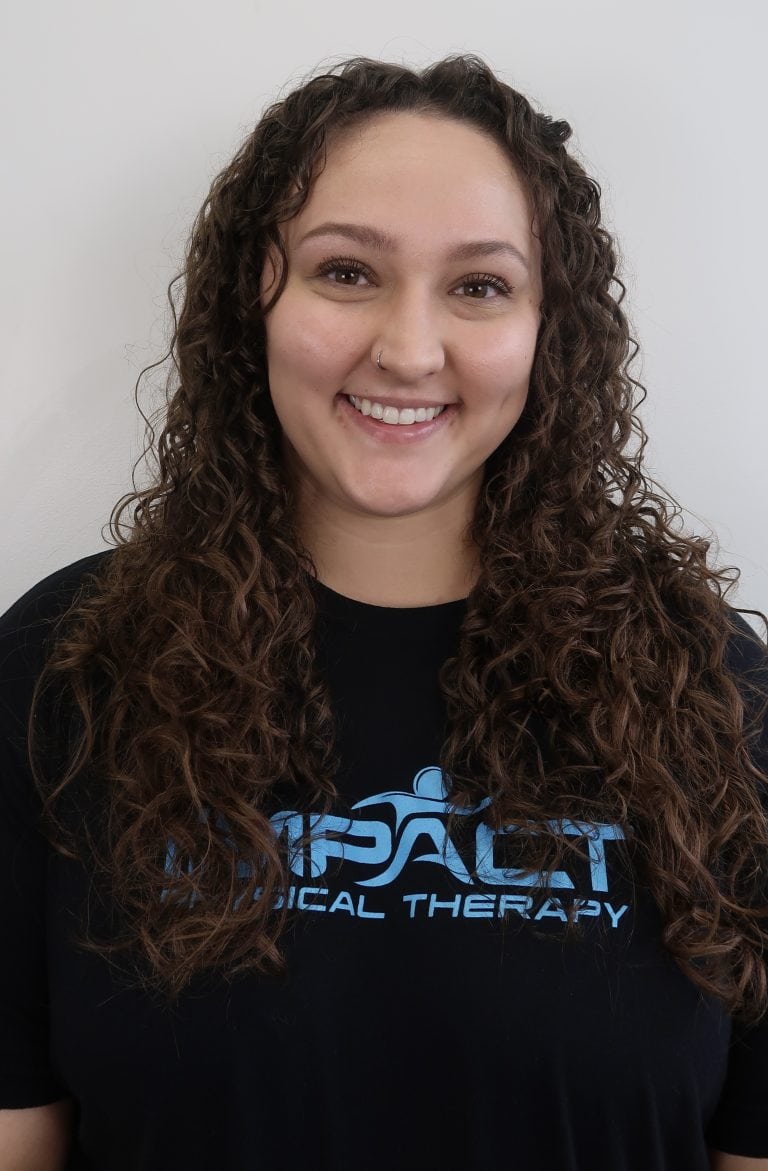 Smiling woman in Impact Physical Therapy T-shirt with curly hair.