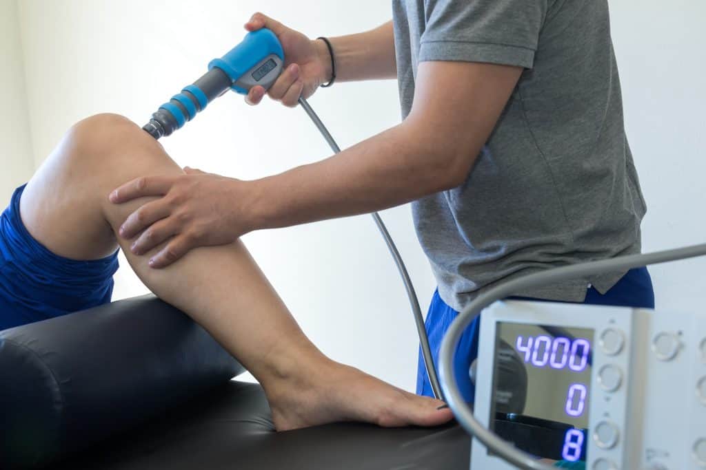 Physical therapist applying shockwave therapy to patient's knee.