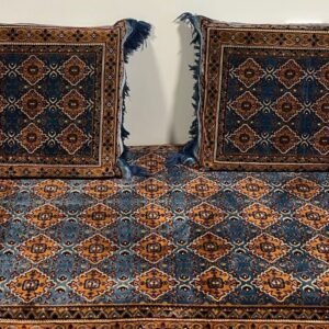 Cushions and rug with blue-orange geometric pattern, fringed edges, on wooden floor.