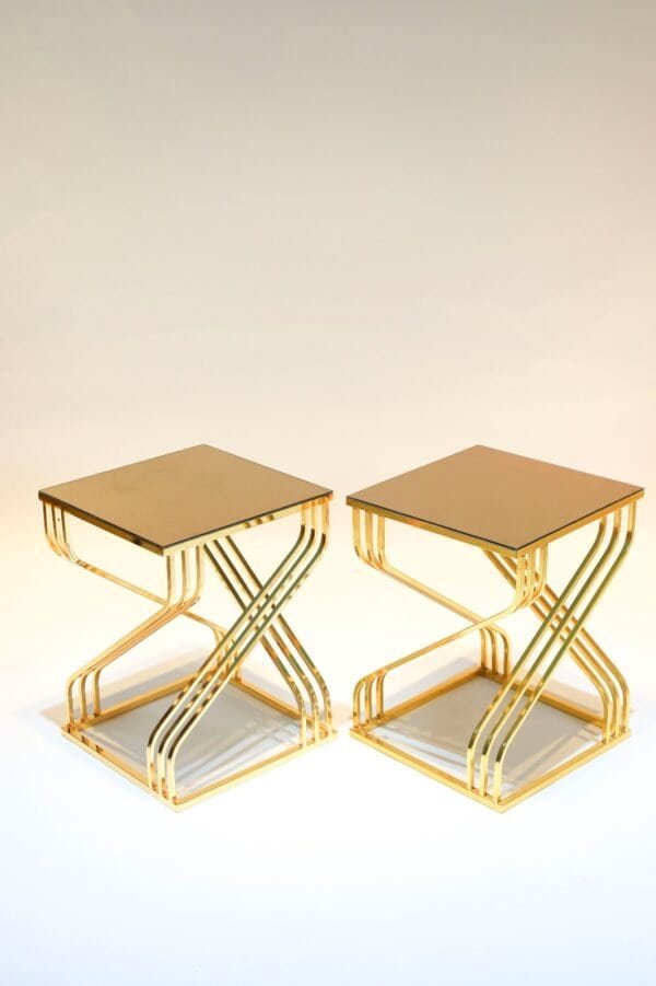 Two Gold Tables With Glass Tops, Featuring Intertwined X-Shaped Metal Supports.