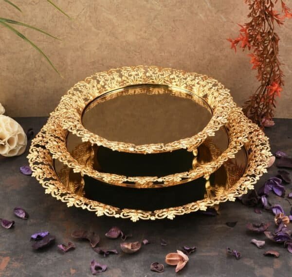 Two-Tiered Gold Display Stand With Floral Designs, Dried Petals, And Plants Against A Textured Wall.