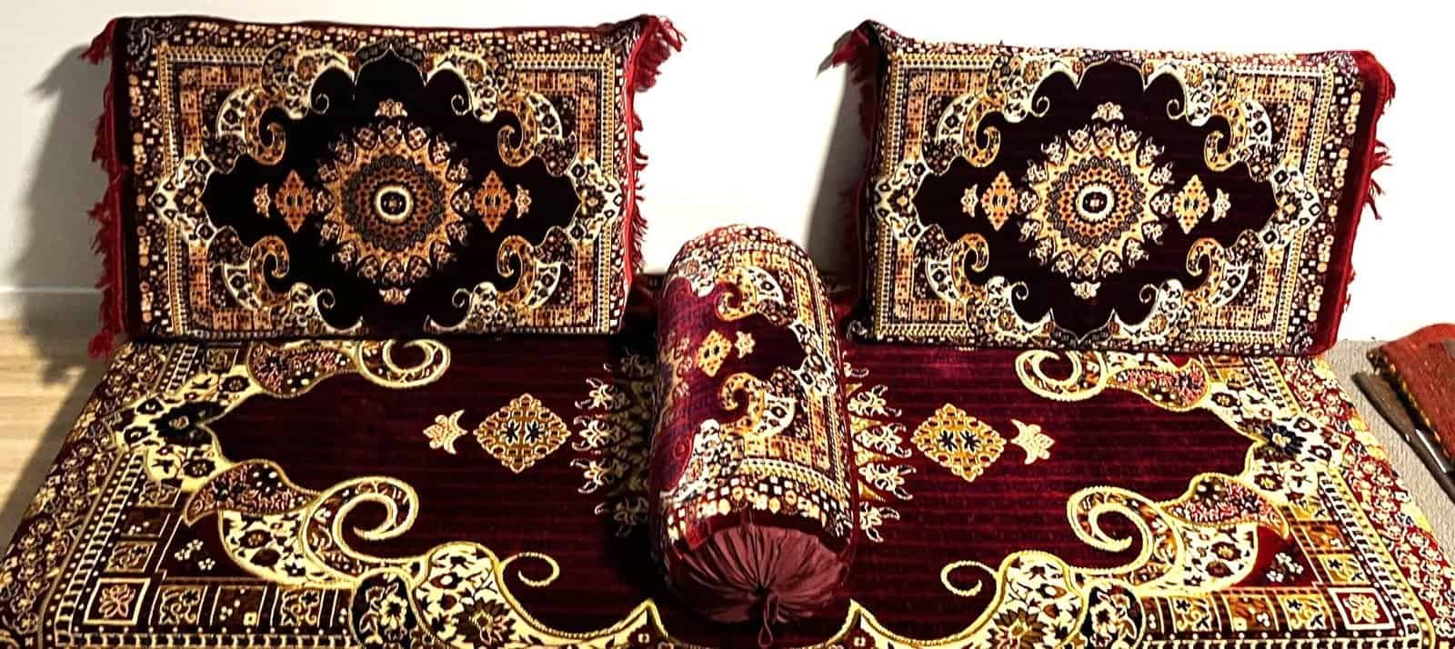 Intricately Designed Cushions And Bolster On A Patterned Carpet With Red And Gold Motifs.