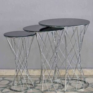 Three round nesting tables with dark glass tops and spiral metal wire bases on a tiled floor.