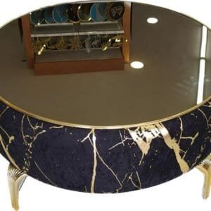 Round coffee table with reflective glass, dark blue and gold pattern, and curved metallic legs.