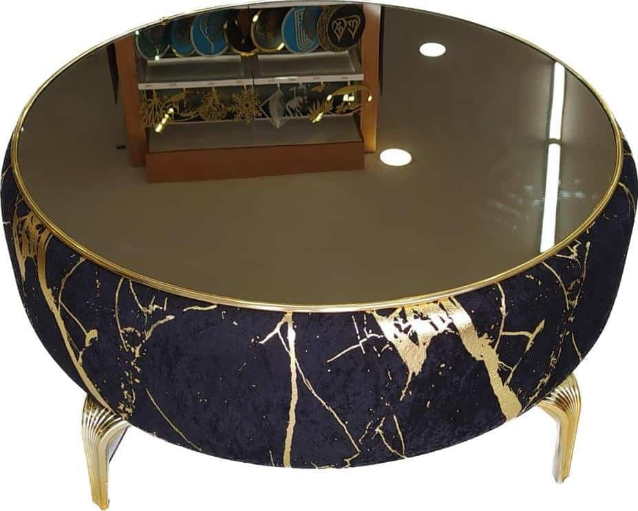 Velvet Puff Tables - The Hero Your New Zealand Home Decor Needs 1 Round Coffee Table With Reflective Glass, Dark Blue And Gold Pattern, And Curved Metallic Legs.