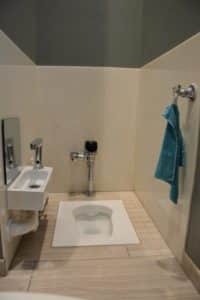 A bathroom with a squat toilet, a small sink with a mirror, and a blue towel hanging on a wall-mounted holder.