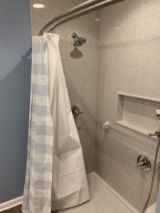 A shower with a partially closed checkered and white shower curtain, wall-mounted showerhead, built-in shelf, and hand-held sprayer.