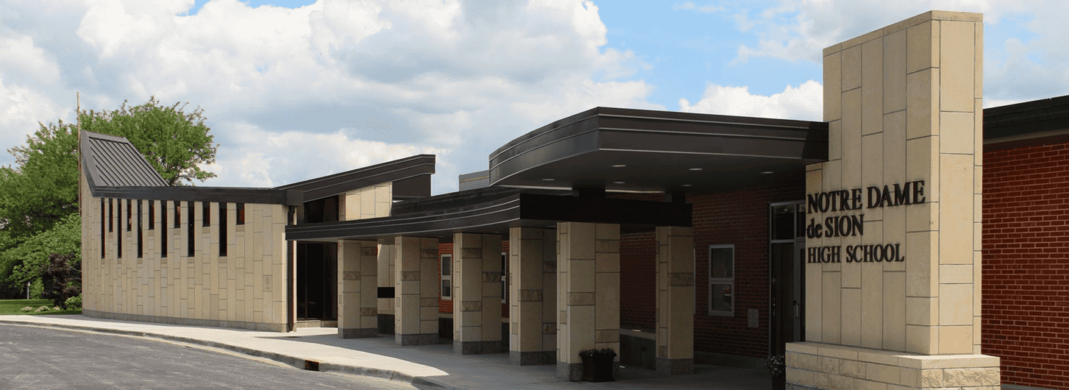 The exterior of Notre Dame de Sion High School, featuring modern architecture with tan stone walls, black trim, and a clear school name sign.