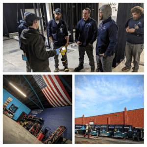 A group of workers talk inside a building, equipment is stored under an American flag, and company vehicles are parked outside a brick building.