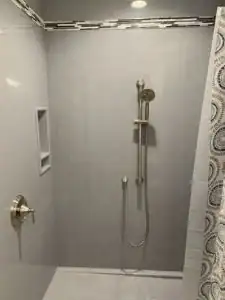 A modern shower with a handheld showerhead, built-in wall shelf, silver fixtures, light gray tiles, and a patterned shower curtain.
