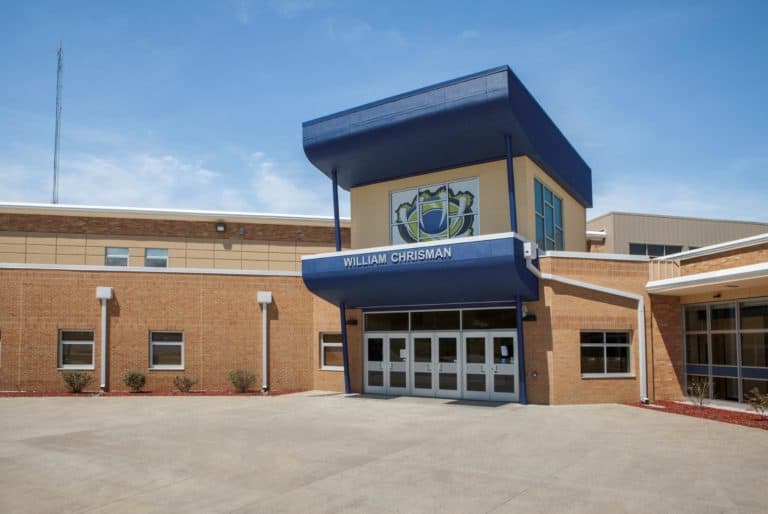 The entrance of William Chrisman High School, featuring a blue awning with the school name and emblem above glass doors, under a clear sky.