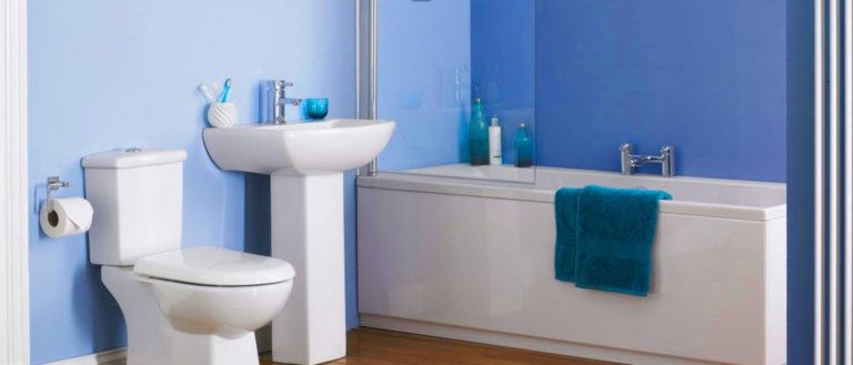 A bathroom with a white toilet, pedestal sink, and bathtub. The walls are light blue, and the tub has blue towels and assorted toiletries.