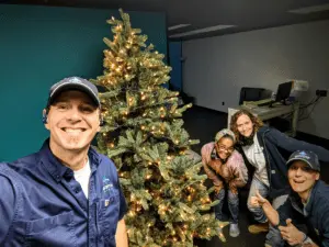 Four people pose and smile near a decorated Christmas tree in an office setting, celebrating the holiday season and the excitement of new careers.
