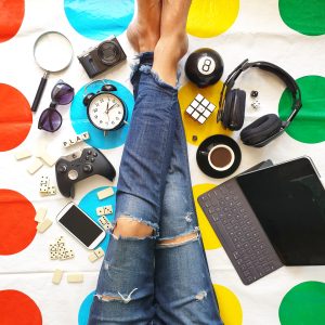 Vibrant flat lay of gaming and entertainment accessories, including a gaming controller, headphones, Rubik's cube, smartphone, and alarm clock, on a colorful polka dot background.