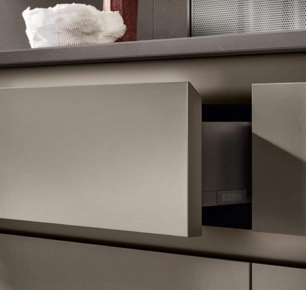 Gray handleless kitchen drawers with a partially opened drawer showing the label &quot;Scavolini&quot; inside.