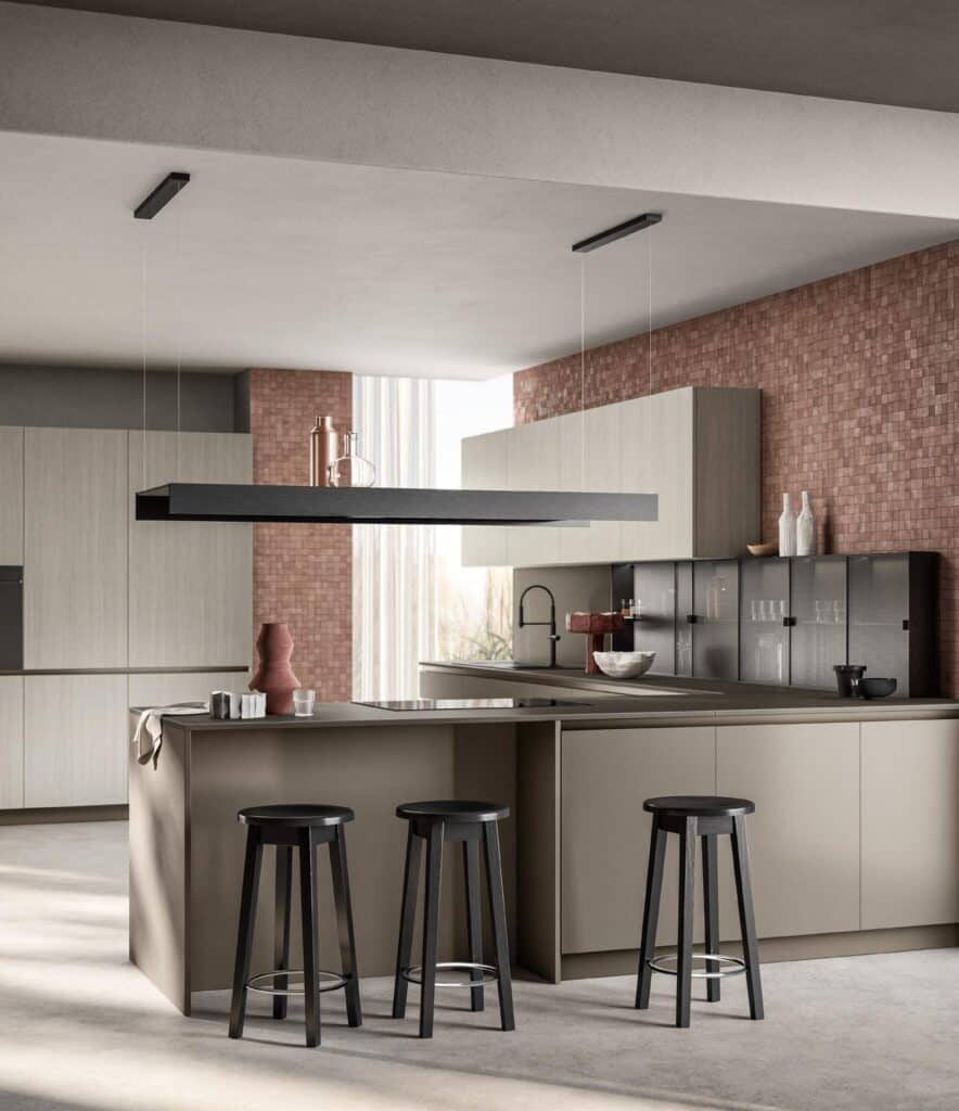 Modern kitchen with beige cabinets, black bar stools, and an island. A minimalist black overhead light fixture and brick backsplash are also visible.