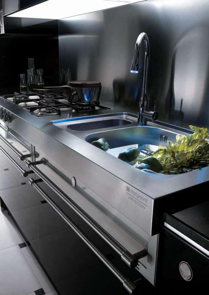 Modern stainless steel kitchen with a gas stove, sink, and faucet; vegetables are in the sink for washing.