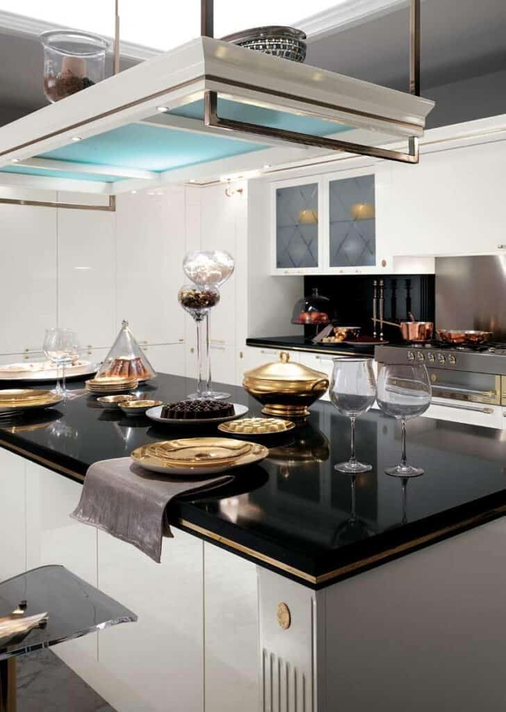 Modern kitchen with glossy black countertops, gold and black dishware, and centerpiece decorations, featuring sleek white cabinetry and a stainless steel stove.