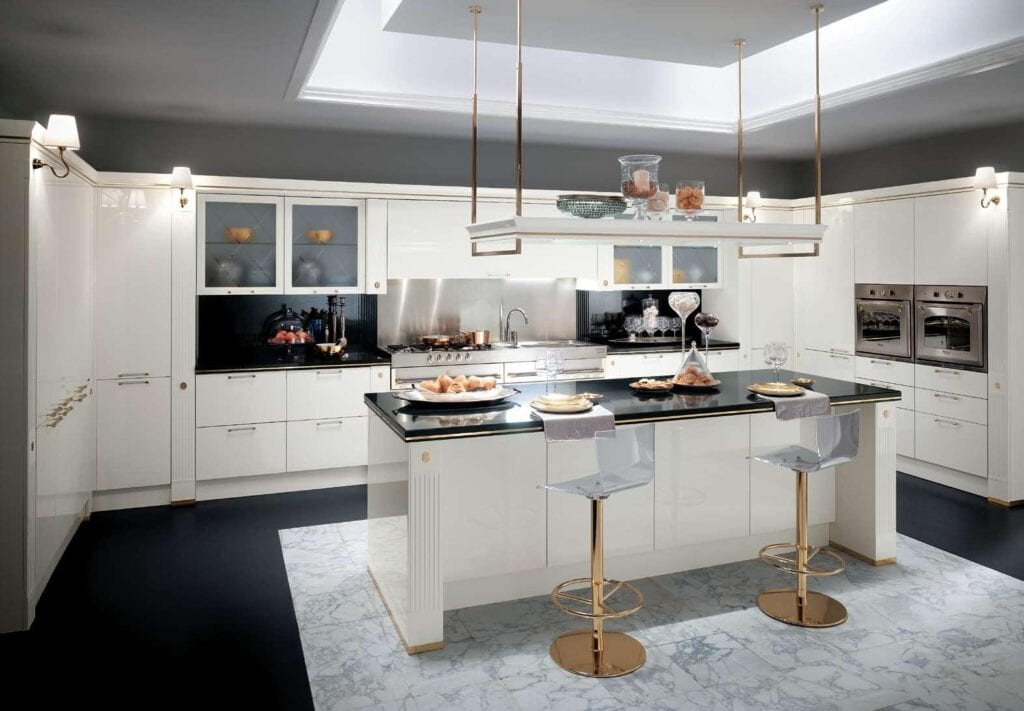Modern kitchen with white cabinets, black countertops, a central island, two transparent bar stools with gold bases, stainless steel appliances, and overhead lighting.