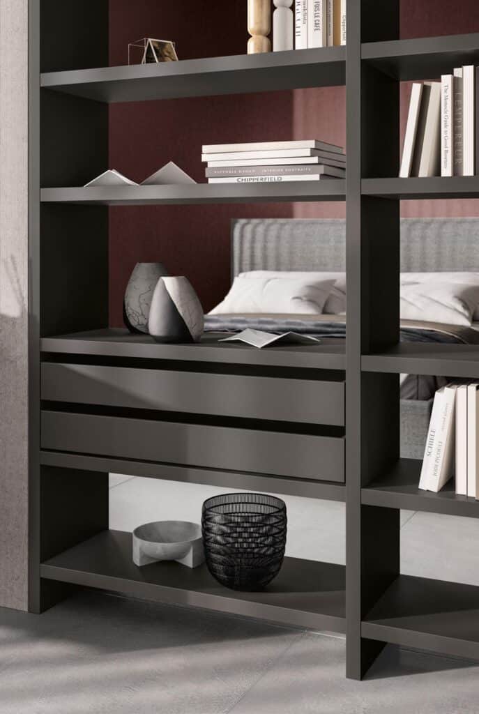 Modern bookshelf with various decorative items, including books, vases, and bowls, partially revealing a bed in the background.