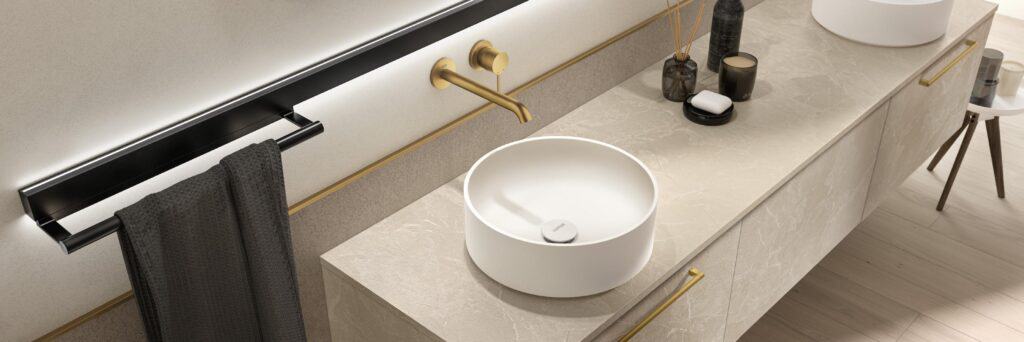Modern bathroom countertop with a round white basin, gold faucet, and decorative accessories.