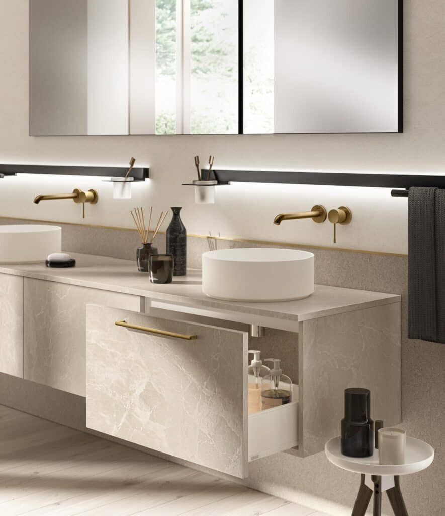 Modern bathroom with double sinks, brass fixtures, and open drawer revealing toiletries.