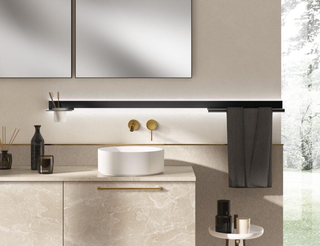 Modern bathroom with a round white sink, brass faucet, marble countertop, and minimalist decor, including a dark towel, toothbrush holder, and candles.
