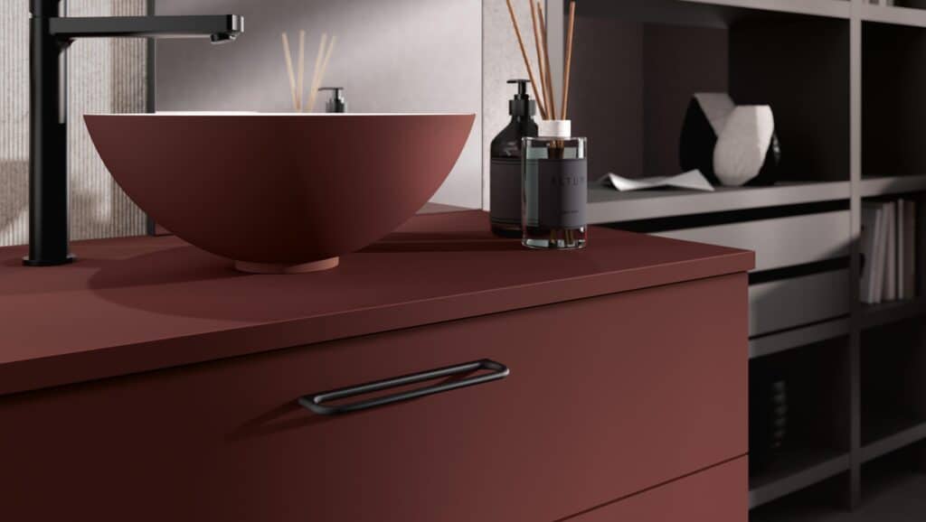 Modern bathroom with a maroon countertop, basin, black faucet, soap dispenser, and reed diffuser.