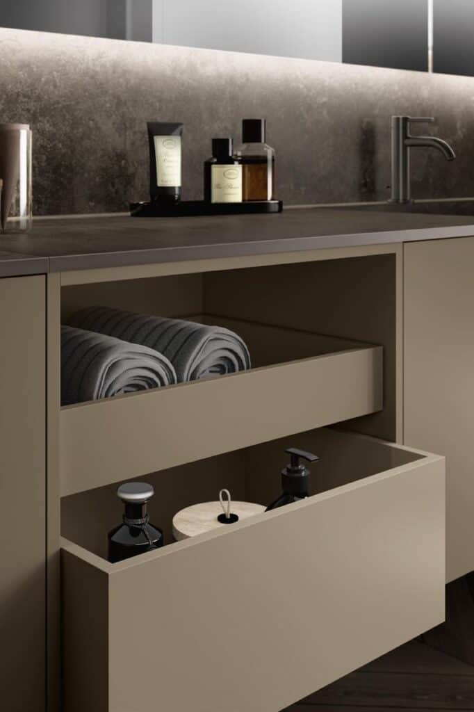 Modern bathroom cabinet with open drawers containing rolled towels and toiletries, alongside a countertop with bottles and a faucet.