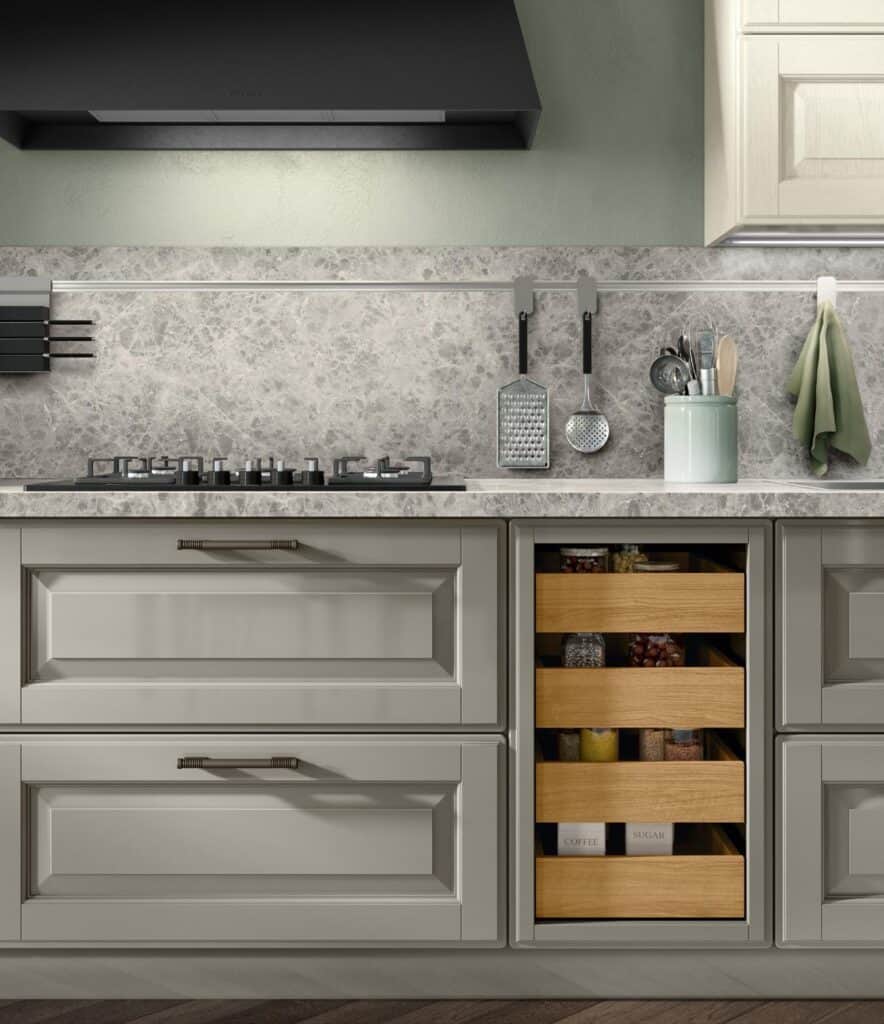 Modern kitchen with light gray cabinets, marble countertop, and backsplash. Black gas stove and extractor fan visible. Wooden shelves with jars and a utensil holder are displayed.