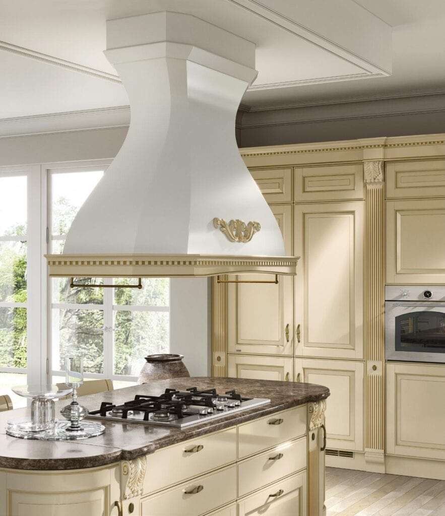 Elegant kitchen with ornate cream cabinetry, marble countertops, and a large white range hood adorned with gold accents.
