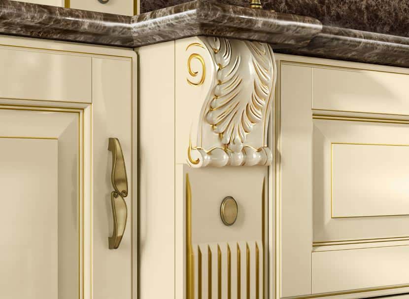 Decorative detail on a cream-colored kitchen cabinet with gold accents and a dark marble countertop.