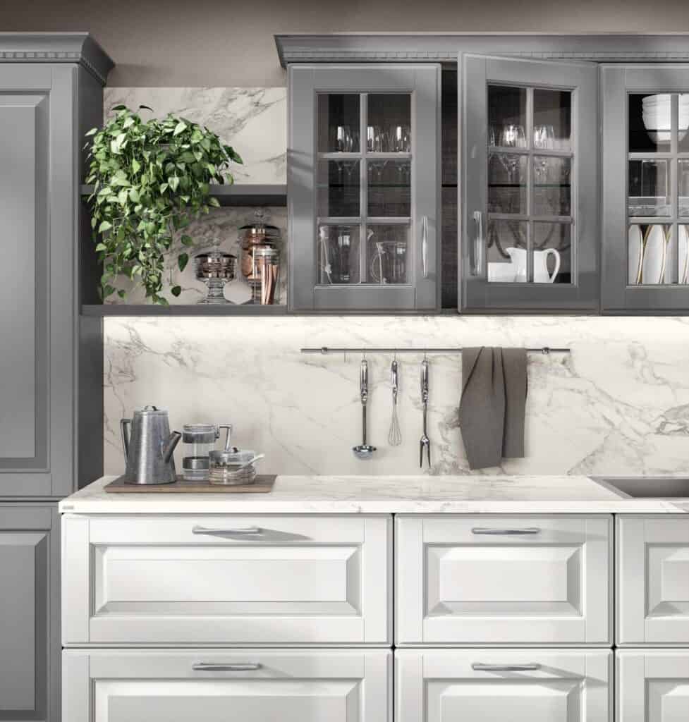 A modern kitchen with gray cabinets, glass doors, a marble backsplash, and countertop. There&#039;s a green plant, glassware, utensils hanging, and a coffee set on a tray.