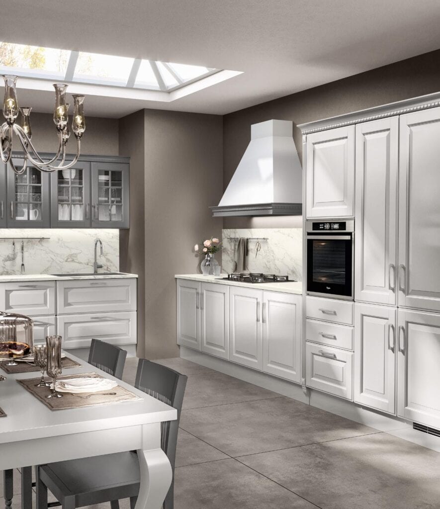 Modern kitchen with white cabinetry, a built-in oven, and a marble backsplash. A table set with glassware is in the foreground, under a chandelier, with a skylight above.
