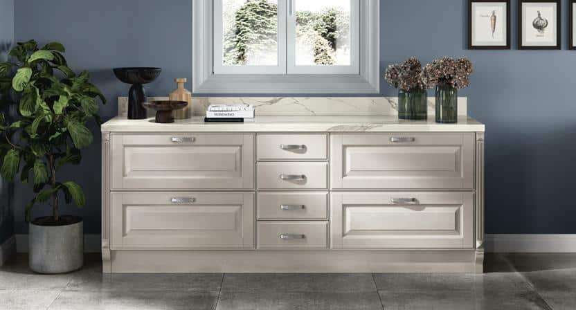 A modern kitchen with an elegant light-colored cabinet, marble countertop, indoor plant, and framed artwork on blue walls.