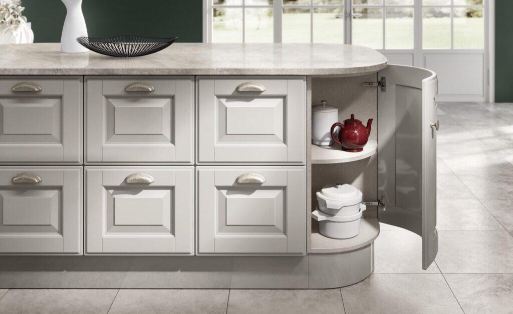 Kitchen island with gray cabinets, a black wire bowl on the countertop, and an open curved cabinet displaying a red teapot and white pots.