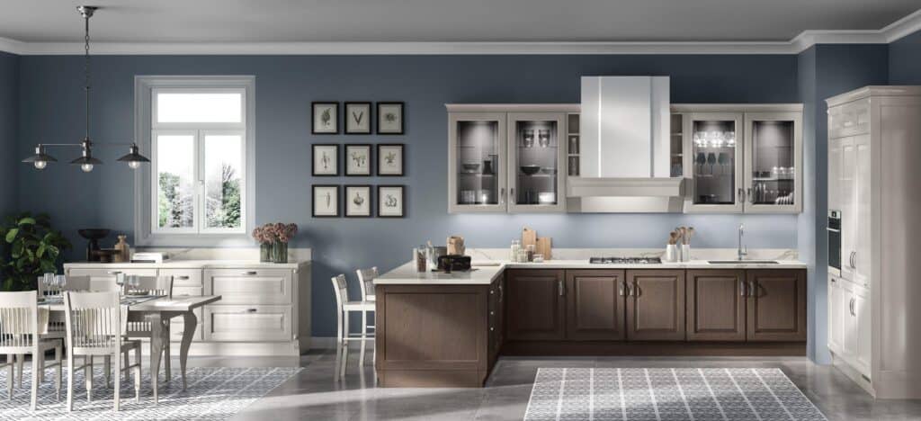 Modern kitchen interior with blue walls, white cabinetry, dark wood accents, dining table with chairs, pendant lighting, and framed botanical prints.