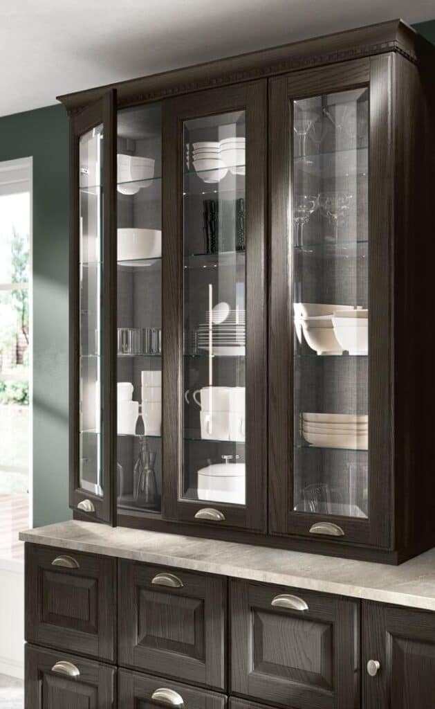 Dark wood kitchen cabinet with glass doors, displaying white dishes, bowls, and glassware on shelves.