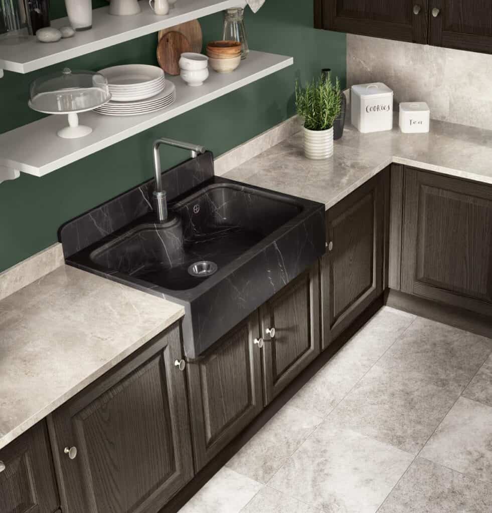 A modern kitchen with dark wood cabinets, black marble sink, white shelving with dishes, and a green wall.