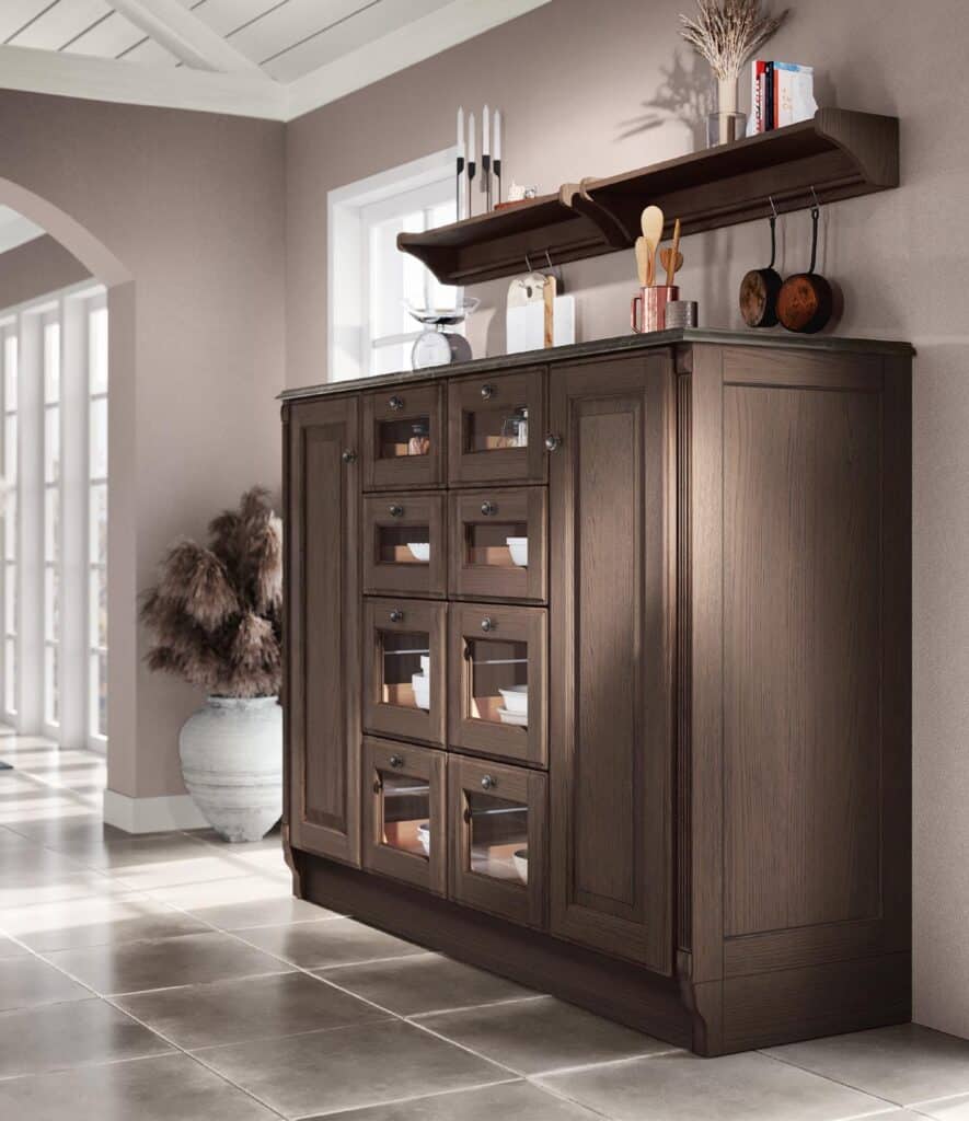 Wooden cabinet with glass-front drawers, a vase of dried plants beside it, and a wall-mounted shelf holding decor and kitchen items.