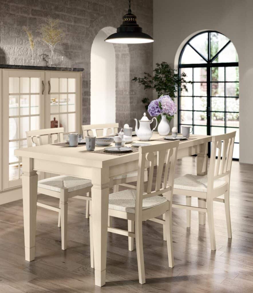 Dining room with a wooden table set, chairs, tea set, and purple hydrangeas, under a hanging lamp near an arched window.