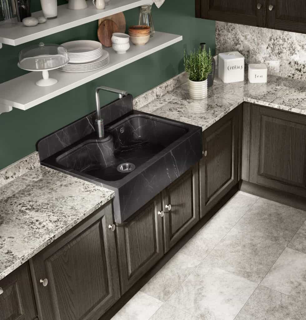Modern kitchen with dark marble sink, gray cabinets, marble countertops, green walls, and open shelves displaying dishes and decor.