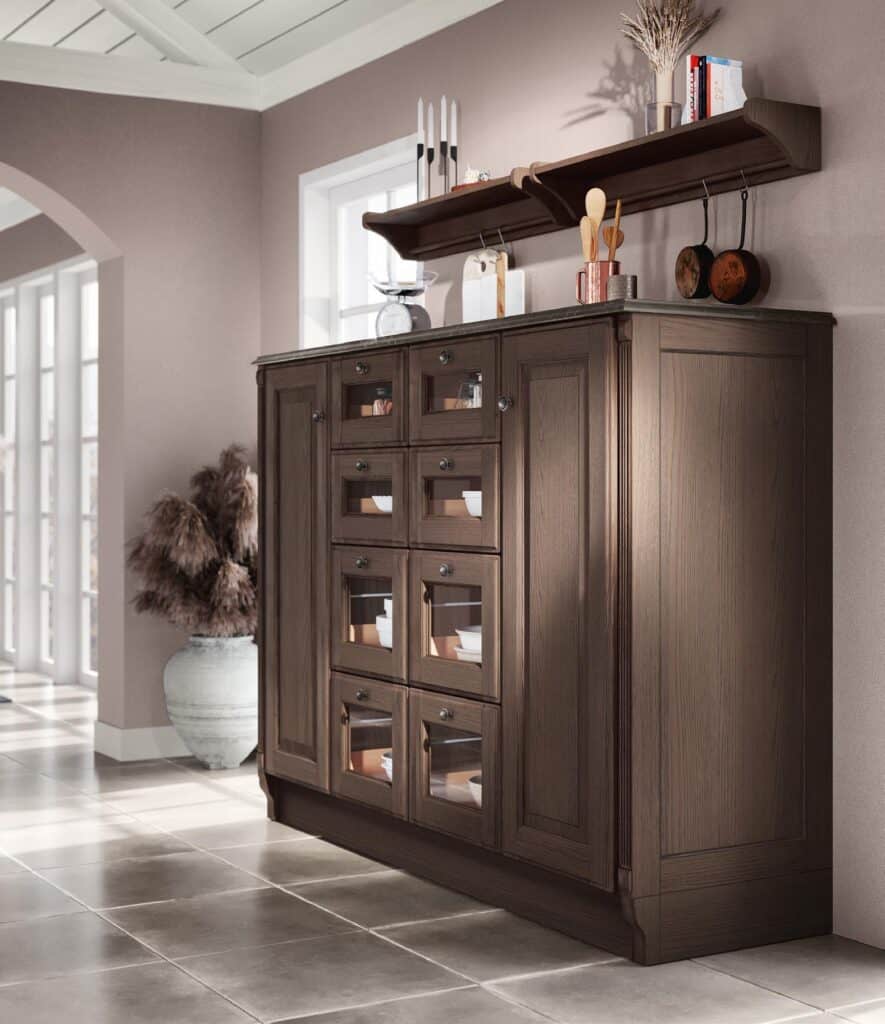 Wooden cabinet with glass doors and a shelf above, holding kitchen items in a room with large windows and potted plant.