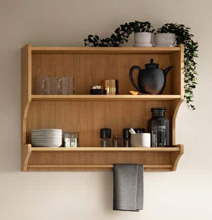 Wooden wall shelf with kitchen items, including mugs, glasses, plates, a teapot, spice jars, and a black towel hanging below.