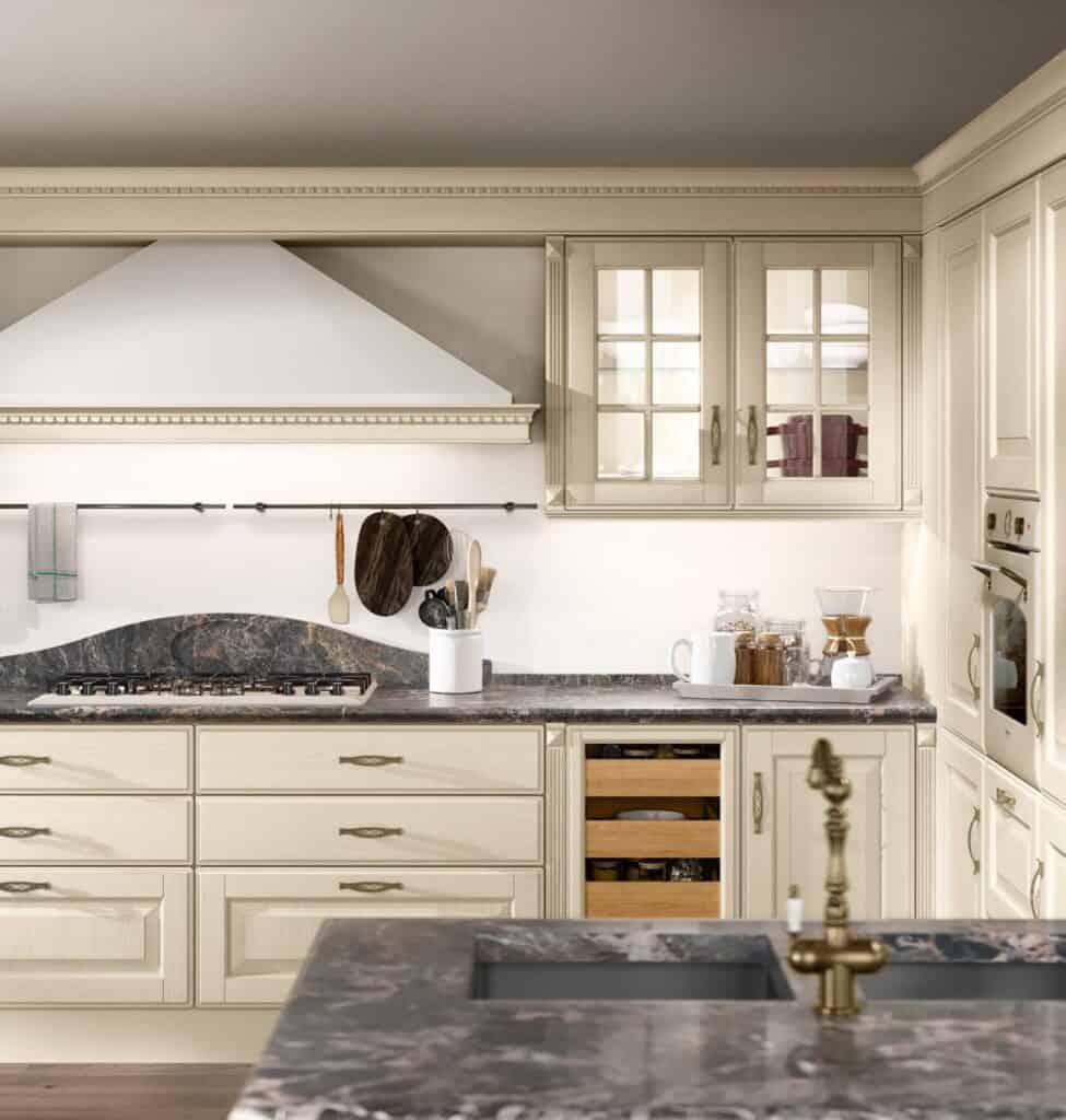 Traditional kitchen with cream cabinets, marble countertops, and brass fixtures, featuring a gas stove, glass-front cabinets, and various kitchen utensils.