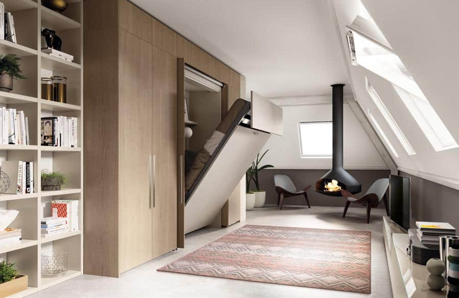 A modern living space with a fold-down bed integrated into a wooden wall panel, an open shelving unit, a ceiling-mounted fireplace, two chairs, and a patterned rug under angled skylight windows.